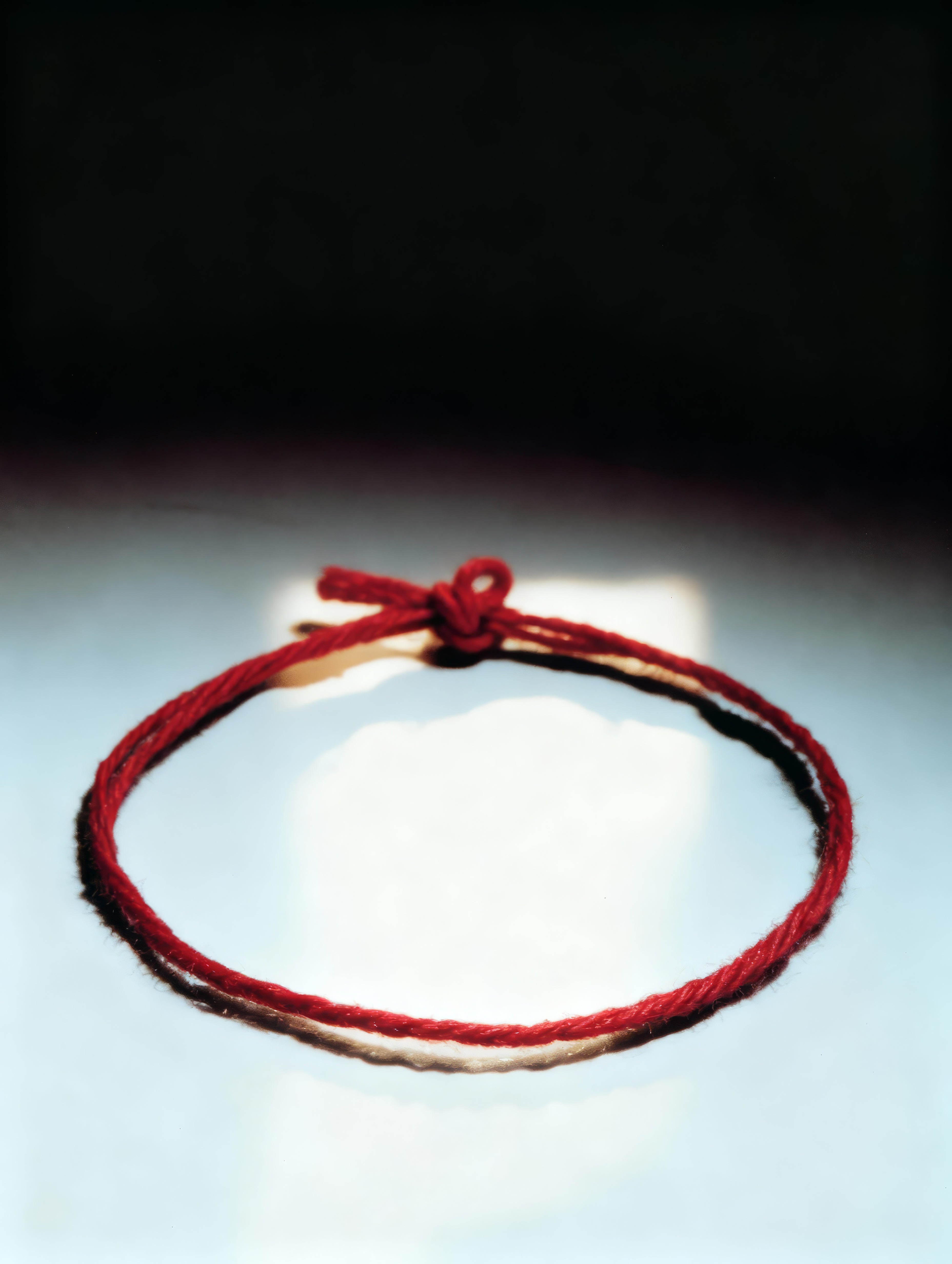 Red string bracelet on a reflective surface with a dark background